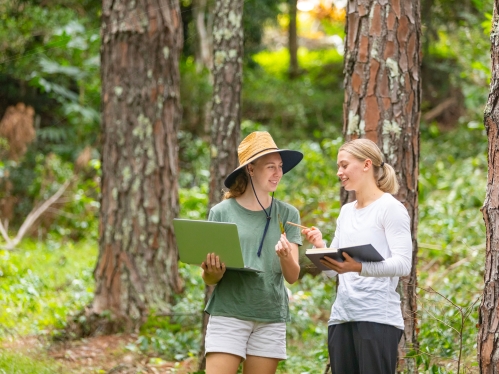Two students taking notes of observations in a forested area